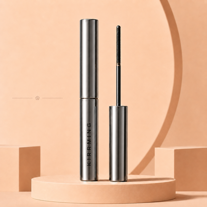 A silver cosmetic tube and its applicator wand standing upright on a beige pedestal against a warm beige studio background. The tube is labeled KIRMING.