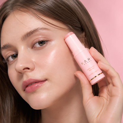 Person applying KAHI Wrinkle Bounce Multi Balm to the cheek in a soft pink skincare application image.